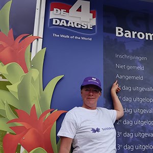 Gezonde vrouw wijst naar informatiebord over schildklierziekten tijdens de 4-daagse wandeltocht in Nederland.
